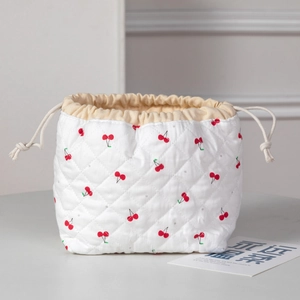 Close-up of quilted drawstring cosmetic bag featuring cute red cherry patterns and textures