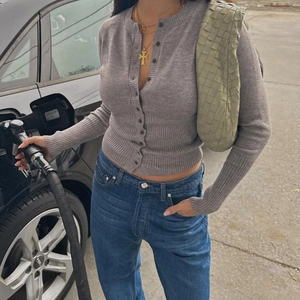 Close-up of a grey slim-fit knitted cardigan with button detail and a green woven handbag