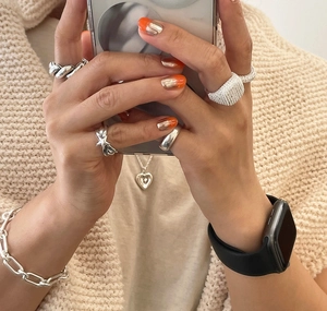 Close-up of minimalist 925 sterling silver heart rings and layered jewelry on a beige knit