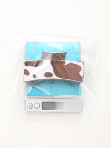 Detail shot of a large cow print hair claw clip weighing 26.3g on a digital scale