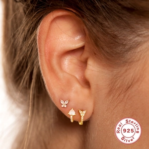 Detailed close-up of 925 sterling silver butterfly, heart and leaf earrings set on ear