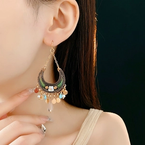 Macro detail of Bohemian moon earrings with green enamel and golden tassel charms
