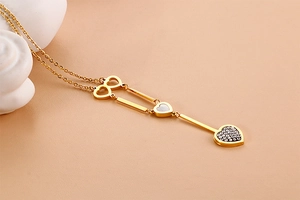 Macro shot of gold heart necklace with mother of pearl and crystal charms on pink background