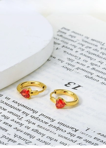 Close-up of heart-shaped red zircon earrings with gold titanium steel hoop on book pages