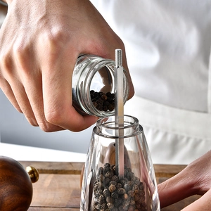 Acacia wood and acrylic pepper grinder being filled with fresh black peppercorns