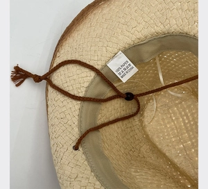 Detail of straw cowboy hat interior showing 100% paper material label and chin strap