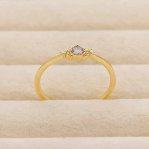 Detail of a thin gold band ring with a round lavender gemstone and tiny side stones