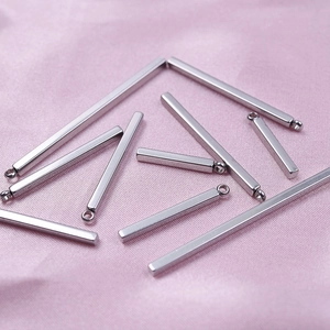 Detailed view of silver stainless steel bar pendants on pink silk fabric background
