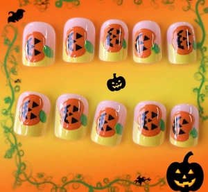 Detail of Halloween press-on nails featuring orange pumpkin patterns on pink base