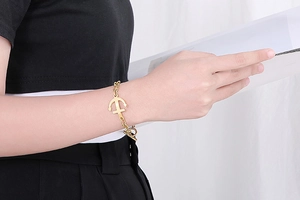 Detailed view of a gold anchor pendant bracelet with OT toggle clasp on a stylish model