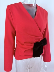 Detail of red slim-fit top featuring deep V-neck and a large black velvet bow at the waist