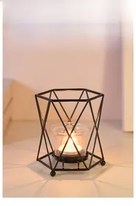 Close-up of geometric black iron candle holder with warm lit candle inside