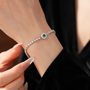 Detail of silver tennis bracelet with a green stone flower charm on a model's wrist