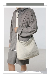 Male model styling a large beige nylon crossbody messenger bag in a minimalist techwear look