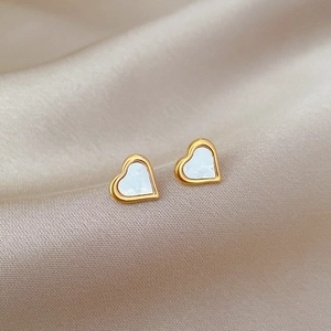 Close-up of minimalist heart stud earrings with white shell inlay on soft beige silk background
