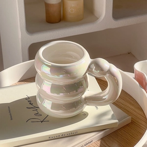 Bubble-shaped white pearlescent ceramic mug with large handle on a wooden tray