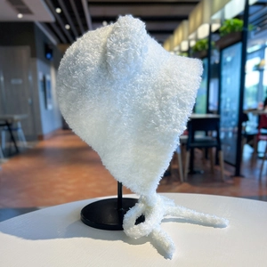 Dettaglio del cappello con orecchie di orso in peluche bianco con lacci su supporto metallico