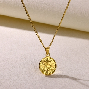 Macro shot of a gold relief praying hands pendant on a Cuban link chain necklace
