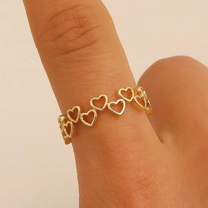 Dettaglio di un anello dorato con motivi a cuore traforati su un dito