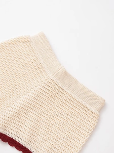 Detail of cream knitted mesh shorts with contrasting red scalloped hem and wavy texture