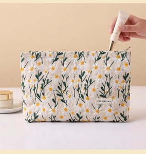 Close-up of beige canvas makeup bag with daisy embroidery and woven brand label