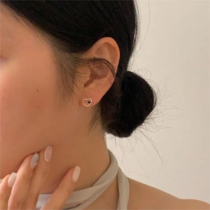 Close-up of minimalist black heart stud earrings with golden trim worn on the ear