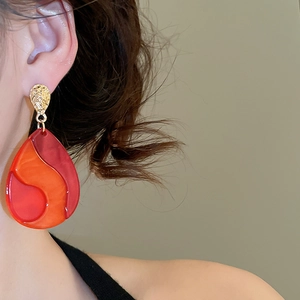 Detailed close-up of water drop earrings with red orange resin inlay and gold hammer texture