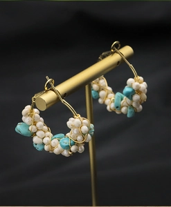 Detail of handmade gold wire hoop earrings featuring natural pearls and turquoise stones