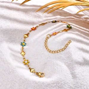Close-up of golden stainless steel chain with colorful enamel flowers on white beach sand