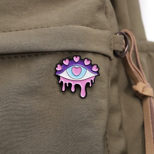 Detailed view of an eye-shaped metal enamel brooch pinned on a khaki green fabric bag