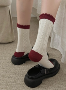Detail of cable knit texture and burgundy ruffle cuff on cream cotton blend socks