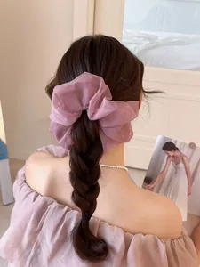 Dettaglio di un elastico per capelli grande in organza viola su una coda a treccia