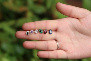 Detailed close-up of six colorful oval gemstone earrings with sparkling diamond halo