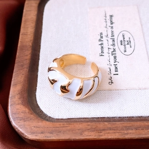 Detail of gold-plated ring with white enamel inlay on a rustic wooden jewelry tray