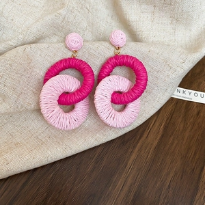 Detail of woven rattan flower earrings in pink and rose red on linen background