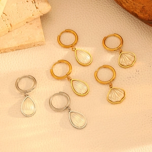 Detail of drop and shell charm earrings in gold and silver finish on stone background