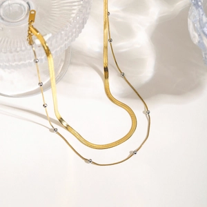 Dettaglio di una catena d'oro a due strati con perle d'argento su sfondo d'acqua ondulata