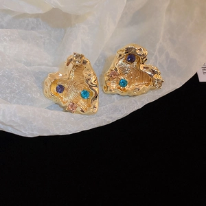 Detailed shot of gold hammered heart earrings with colorful rhinestones on white paper