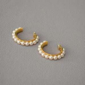 Detail shot of C-shaped gold-plated brass earrings featuring elegant white pearls on a grey background