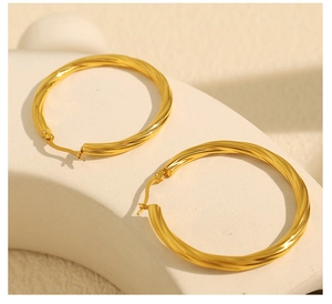 Detail of 18k gold-plated twisted hoop earrings on a beige stand with natural lighting
