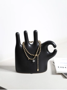 Detail view of a gold bead chain necklace with star pendant on a black ceramic hand stand