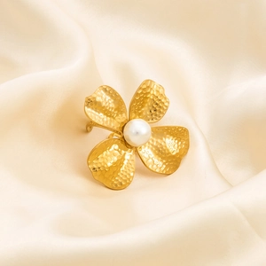 Detail of 18K gold plated stainless steel flower ring with pearl on beige silk fabric