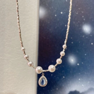 Close-up of pearl necklace featuring a blue teardrop gemstone pendant on starry background