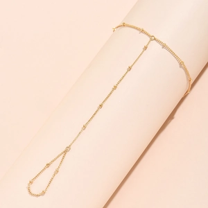 Detail of minimalist gold beaded finger bracelet on a soft pink cylindrical display