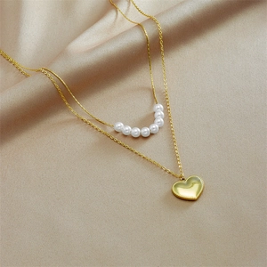 Double-layer gold necklace with white pearls and a heart pendant on beige silk