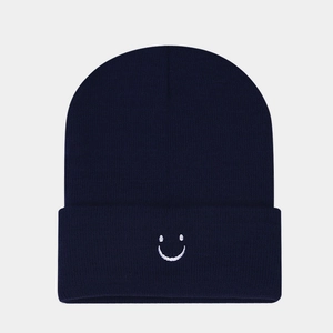 Detail of white smiley face embroidery on a dark blue knitted beanie cuff