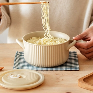 Japanese style beige ceramic noodle bowl with lid and handles on a wooden table