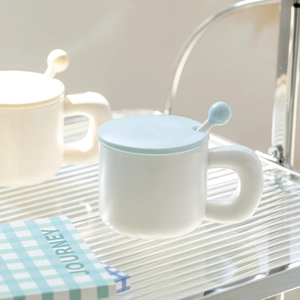 Minimalist white ceramic mug with light blue lid and round handle on a glass shelf