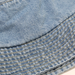 Macro view of blue washed denim fabric with yellow contrast stitching on a bucket hat