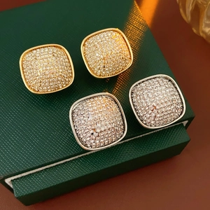 Detailed close-up of square pavé stud earrings in gold and silver plating on green leather